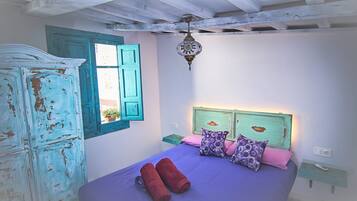 Un dormitorio con cama, armario, ventana con contraventanas azules y una lámpara colgante.