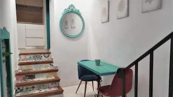 Una escalera con baldosas estampadas, una mesa color turquesa con dos sillas y un espejo decorativo en la pared.