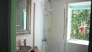 Een badkamer met een douche, een wastafel met een decoratieve kom, een spiegel met een sierlijk frame en een raam met uitzicht op groen.