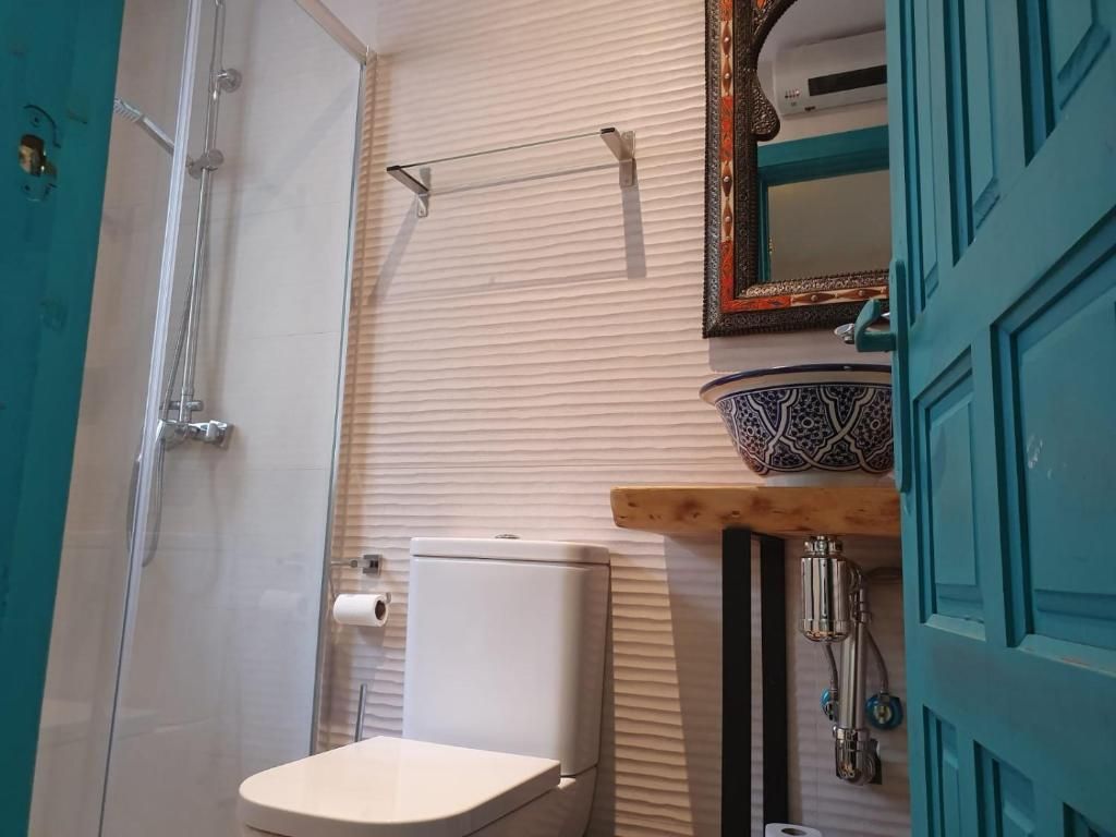 A bathroom with a toilet, a shower, a sink with a decorative basin, and a mirror with a decorative frame.
