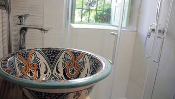 A bathroom with a decorative ceramic sink, a shower, and a window with a view of greenery.