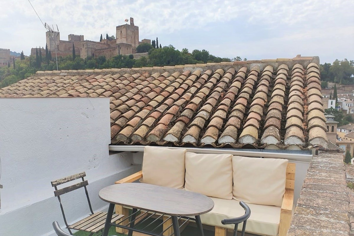 A rooftop terrace with a tiled roof, a sofa, and two chairs.