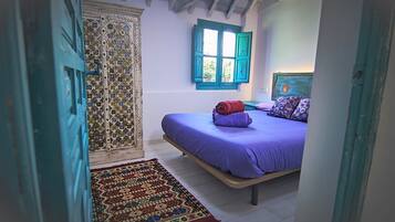 Une chambre à coucher avec un lit, une porte à motifs et une fenêtre avec des volets bleus.