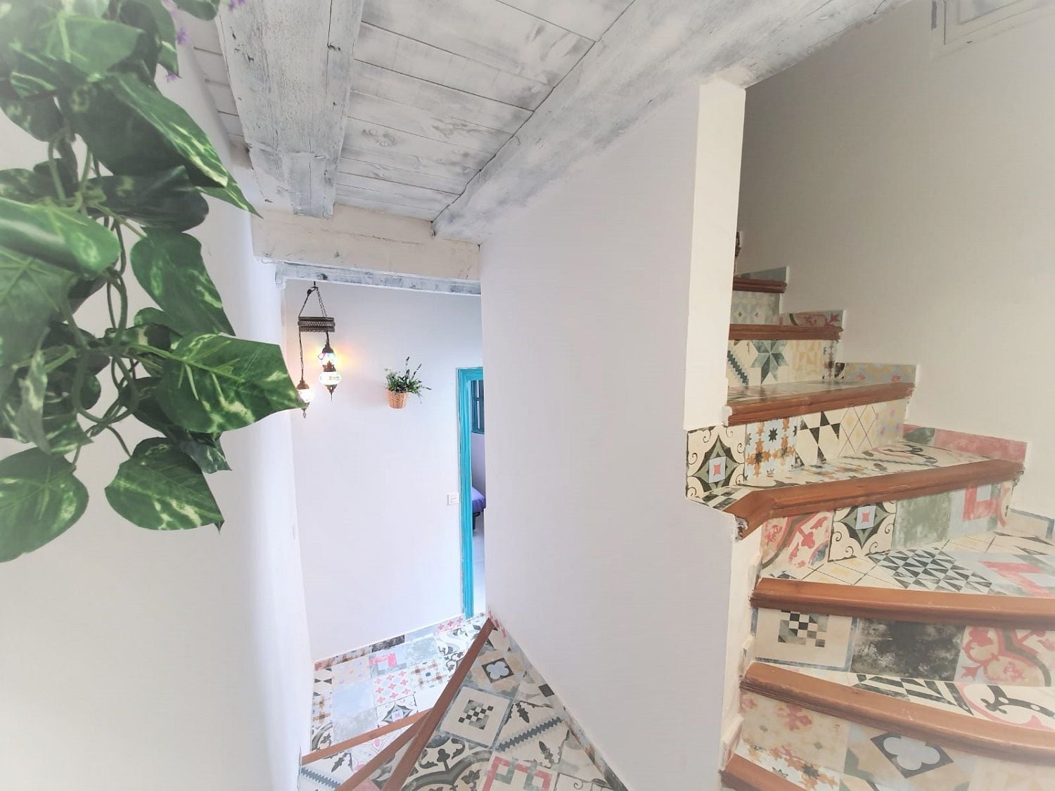 A staircase with patterned tiles and a wooden handrail, leading to a room with a blue door.