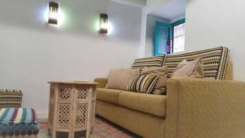 Un salon comprenant un canapé, une petite table en bois et deux lampes fixées au mur.