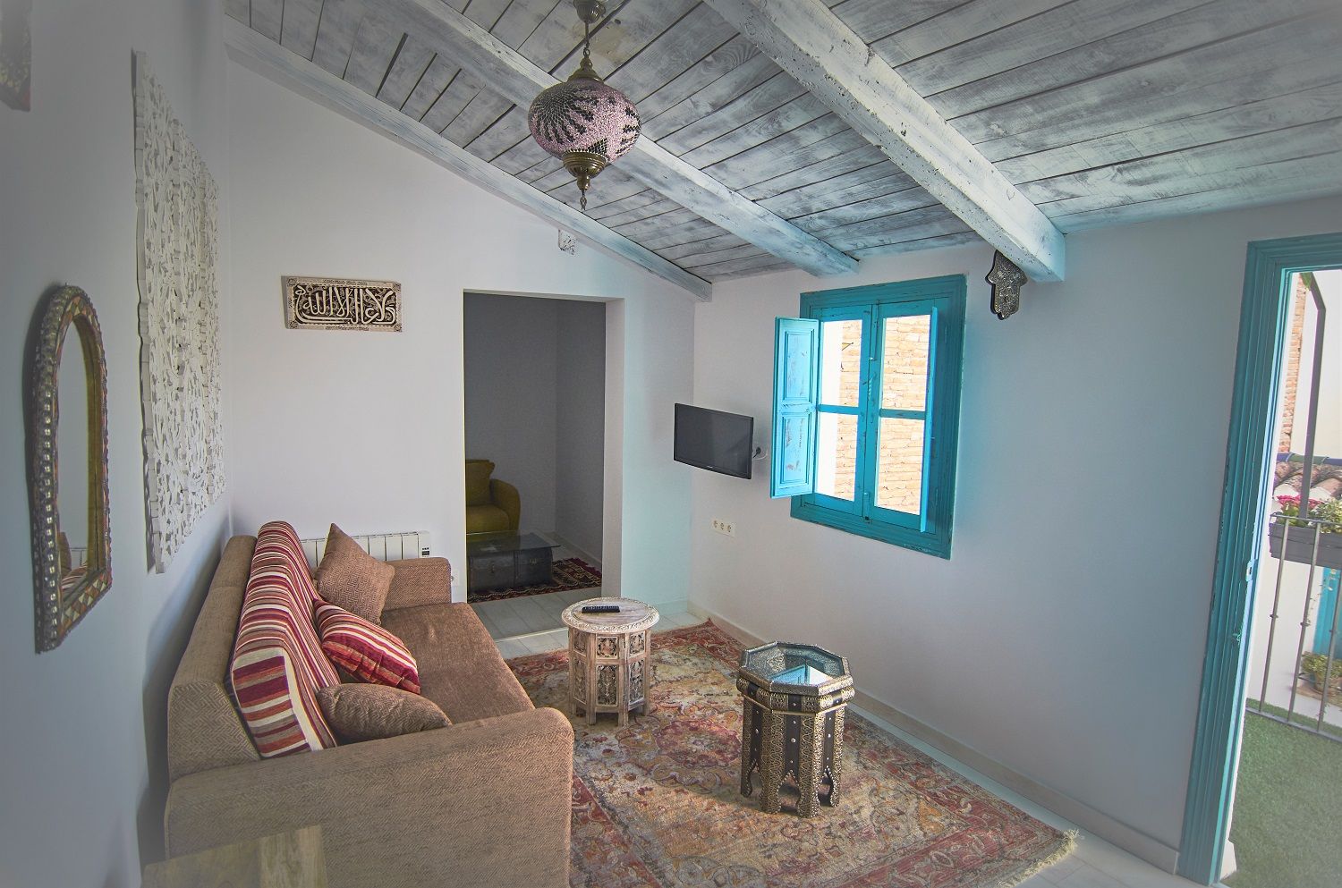 A living room with a sofa, a patterned rug, a decorative lamp, and a window with blue shutters.