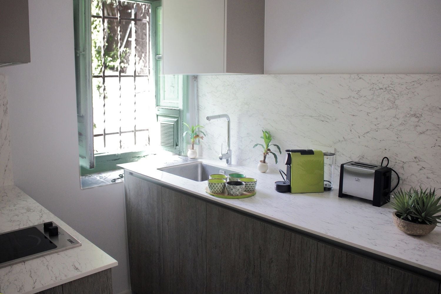 Una cocina con un lavamanos, un tostador y una ventana con vistas a la vegetación.