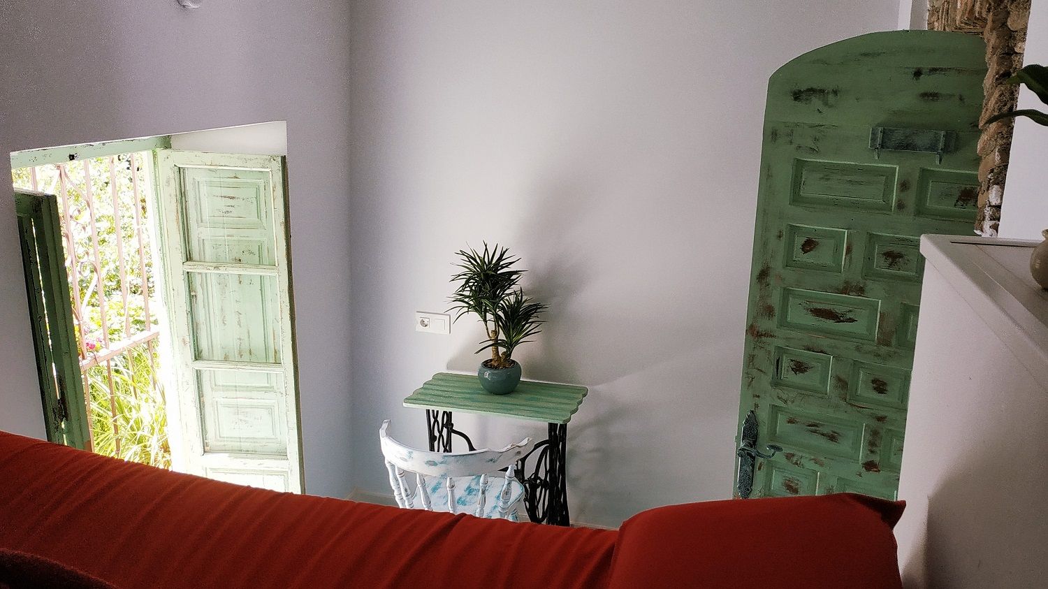 Una habitación con un sofá rojo, una mesita con una planta y dos puertas verdes.