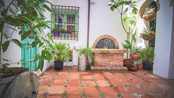 A courtyard with a tiled floor, potted plants, a brick wall, and a window with a metal grille.