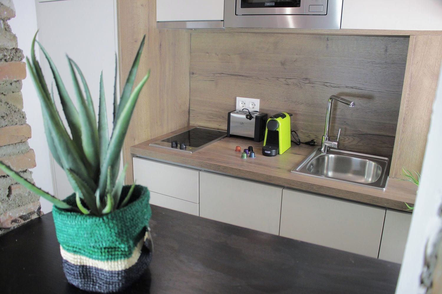 A kitchen with a wooden countertop, a sink, a microwave, and a potted plant.