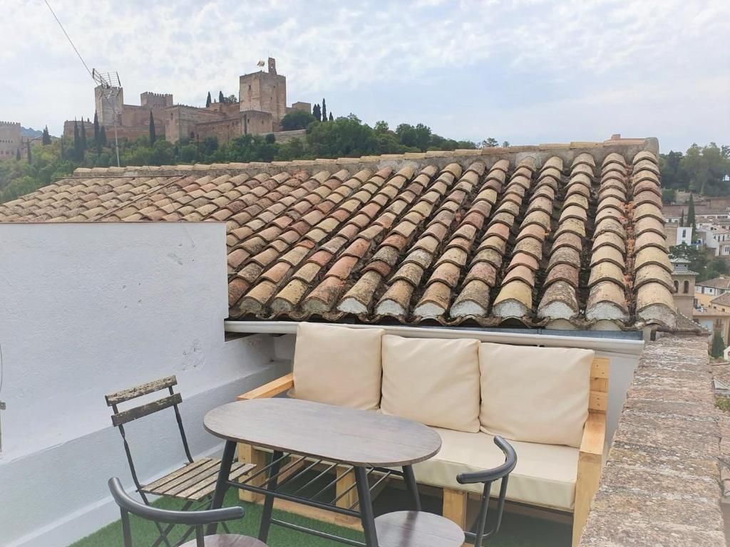 A rooftop terrace with a table and chairs, a cushioned bench, and a view of a historic castle.