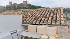 Een terras op het dak met een tafel, stoelen en een comfortabele bank, met uitzicht op een historisch kasteel.
