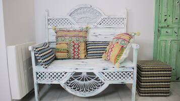 A white, distressed wooden bench with intricate carvings and multiple colorful cushions.