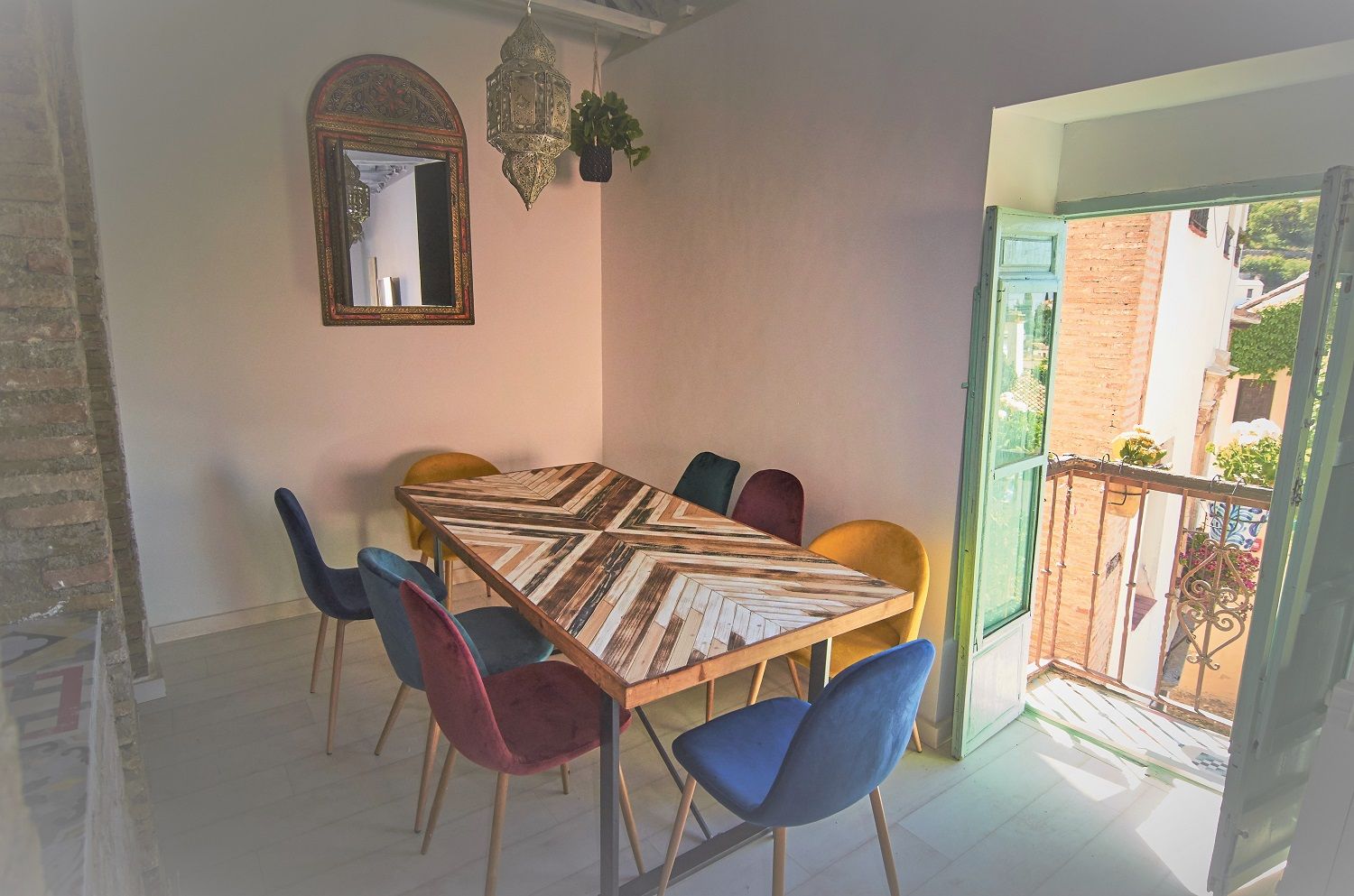 A dining area with a large wooden table, colorful chairs, a hanging lantern, and a mirror on the wall.