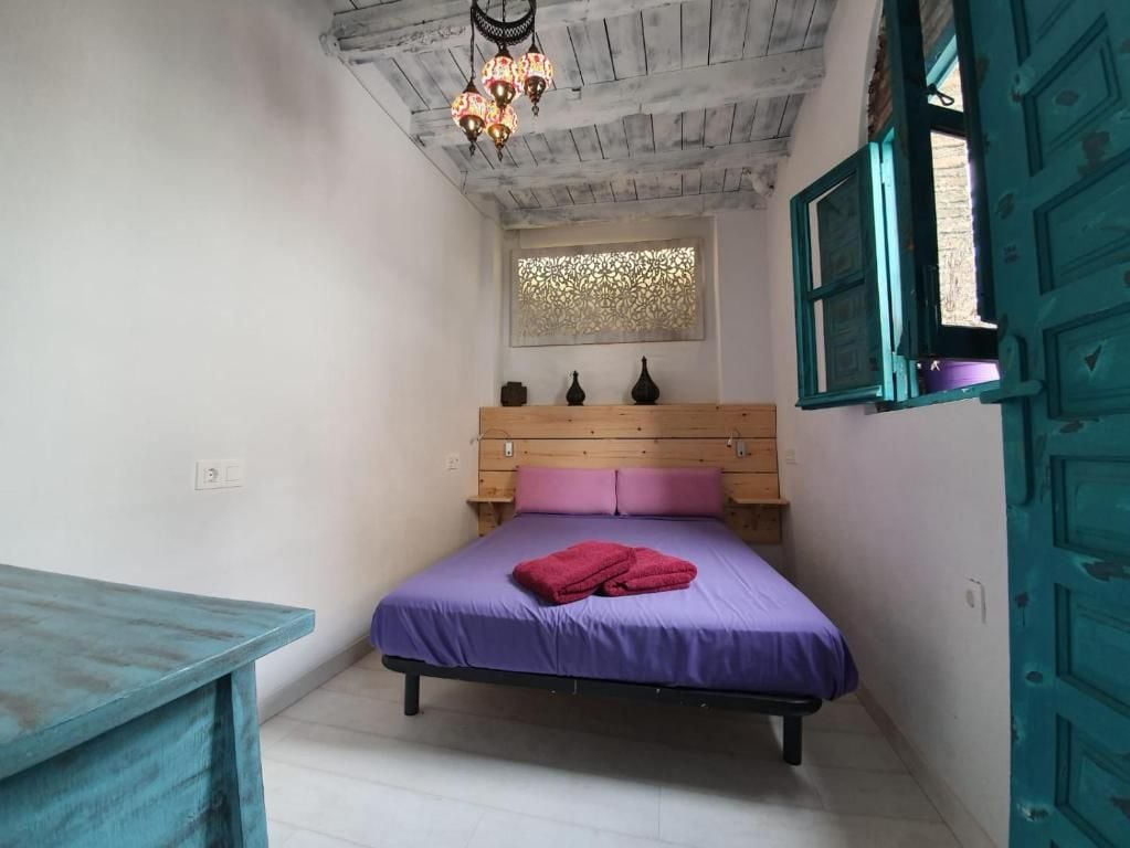 Un dormitorio con una cama de madera, una mesita de noche pequeña, un panel decorativo en la pared y una puerta color turquesa.
