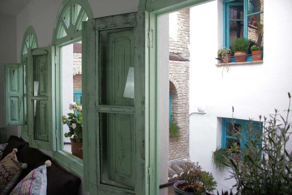 Una habitación con puerta verde, ventana con contraventanas azules y una planta en maceta en el alféizar.