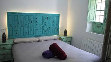 Una cama con sábanas blancas, un cabecero color turquesa y dos toallas enrolladas.