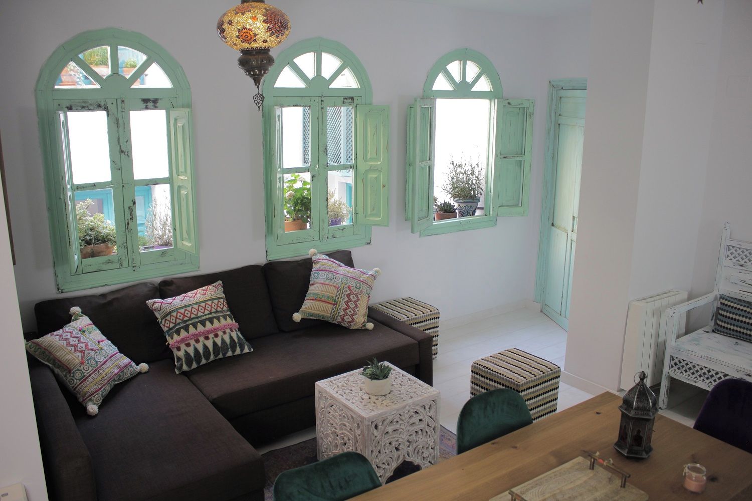 A cozy room with a brown sofa, patterned cushions, a small table with a potted plant, and a decorative hanging light.