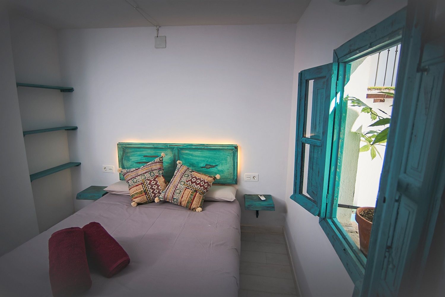A bedroom with a bed, two bedside tables, a window with a view, and a headboard with a painted design.