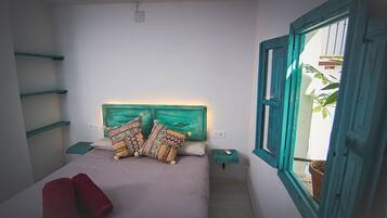 A bedroom with a bed, two bedside tables, a window with a view, and a headboard with a painted design.