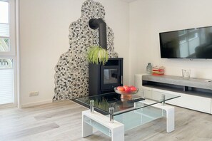 Una sala de estar moderna con una mesa de centro de vidrio, un estufa de leña negra, un televisor de pantalla plana y una pared de mosaicos de piedra.