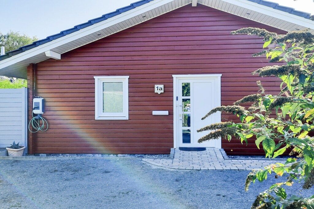 Ein rotes Holzhaus mit einer weißen Tür und einem Fenster, einem Briefkasten und der Hausnummer '1a' an der Wand.