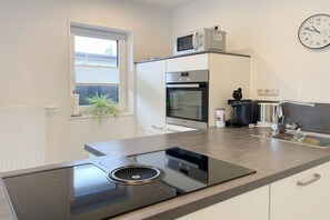 A modern kitchen with a built-in stove, oven, microwave, and a clock on the wall. - Holiday home with 2 bedrooms (Timmendorfer Strand)