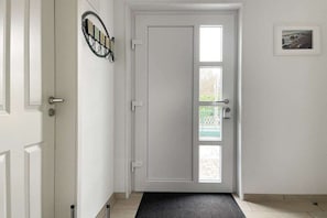 Una puerta blanca con felpudo negro, un aplique de pared y un cuadro enmarcado.