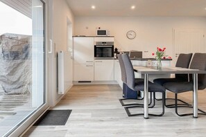 A modern kitchen with white cabinets, a microwave, and a clock on the wall. - Holiday home with 2 bedrooms (Timmendorfer Strand)