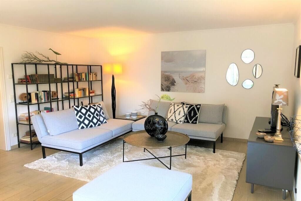 A modern living room with a sectional sofa, a coffee table, a bookshelf, and decorative mirrors.