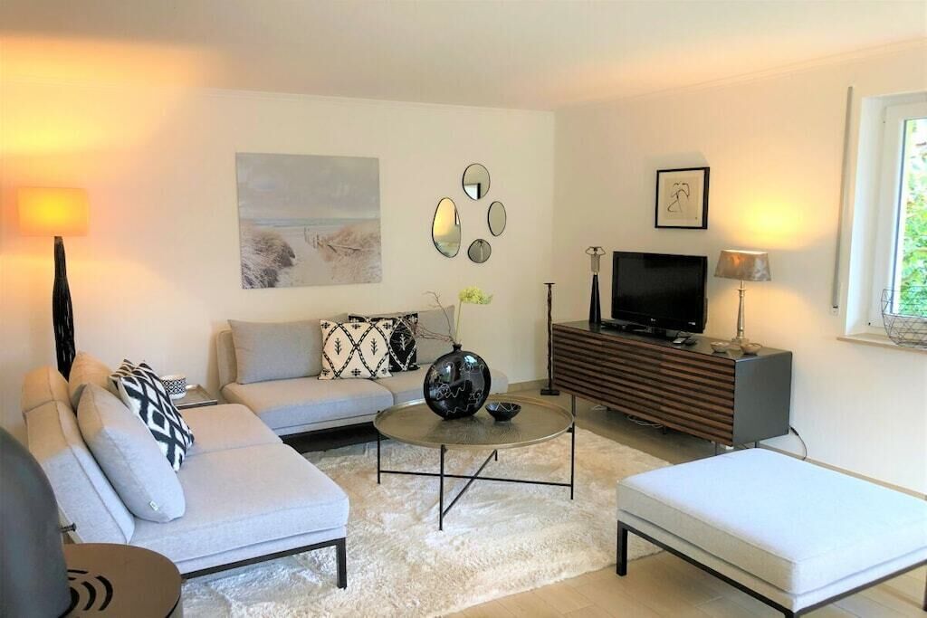 Uma sala de estar moderna com um sofá, uma mesa de centro, uma TV e uma mesinha lateral.