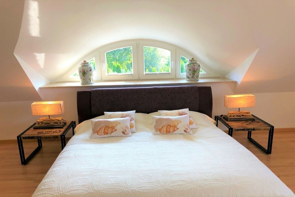 Un dormitorio con una cama grande, dos mesitas de noche con lámparas y un ventanal con vistas al verdor.