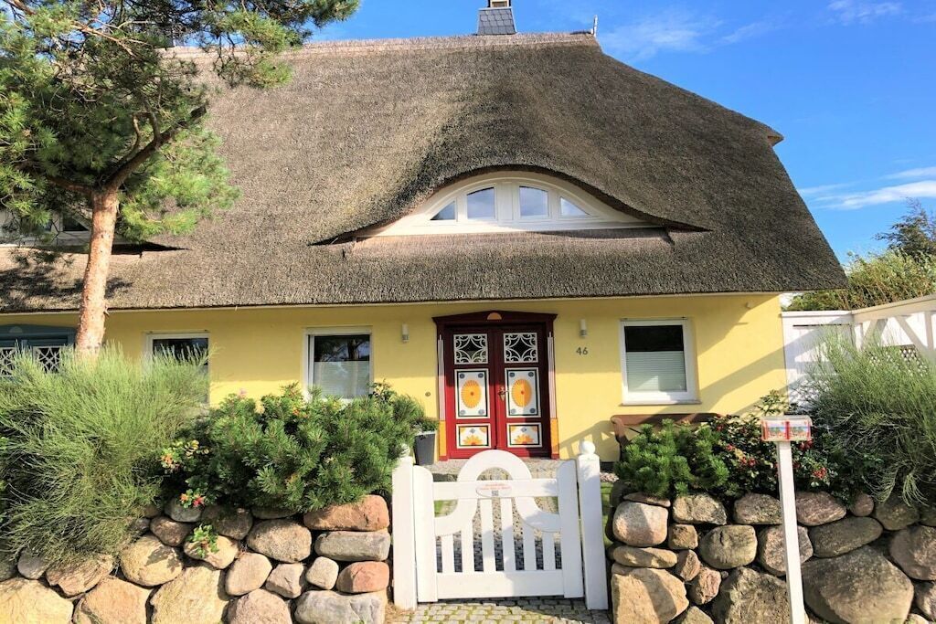 A house with a thatched roof, a yellow facade, and a white gate.