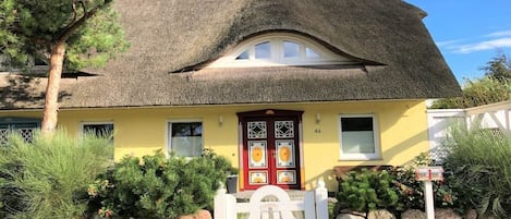 A house with a thatched roof, a yellow facade, and a white gate.