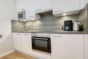 A modern kitchen with white cabinets, a built-in oven, a microwave, and a coffee maker. - Holiday apartment with 1 bedroom (Timmendorfer Strand)