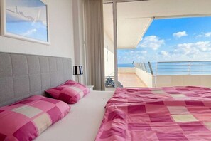 A hotel room with a bed, a window with a view of the sea, and a balcony with a railing. - Holiday apartment with 1 bedroom (Timmendorfer Strand)