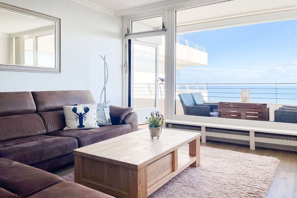 Un salon moderne avec un canapé, une table basse et une vue sur la mer grâce à de grandes fenêtres.