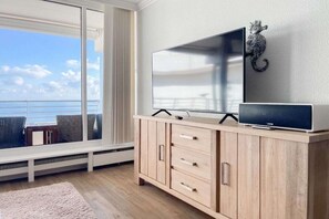 A room with a large window, a flat-screen TV on a wooden cabinet, and a decorative wall piece. - Holiday apartment with 1 bedroom (Timmendorfer Strand)