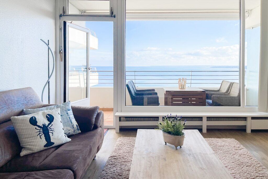 A living room with a sofa, a coffee table, and a view of the sea through a large window.