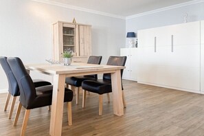 A dining area with a wooden table and black chairs, a cabinet with glass doors, and a white wardrobe. - Holiday apartment with 1 bedroom (Timmendorfer Strand)