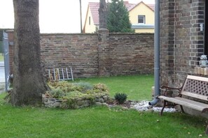 A stone wall, a tree, a bench, and a small garden area. - Holiday apartment with 2 bedrooms (Schönefeld)
