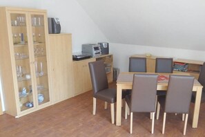 A dining area with a wooden table and chairs, a cabinet with glassware, and a printer on a shelf. - Holiday apartment with 2 bedrooms (Schönefeld)