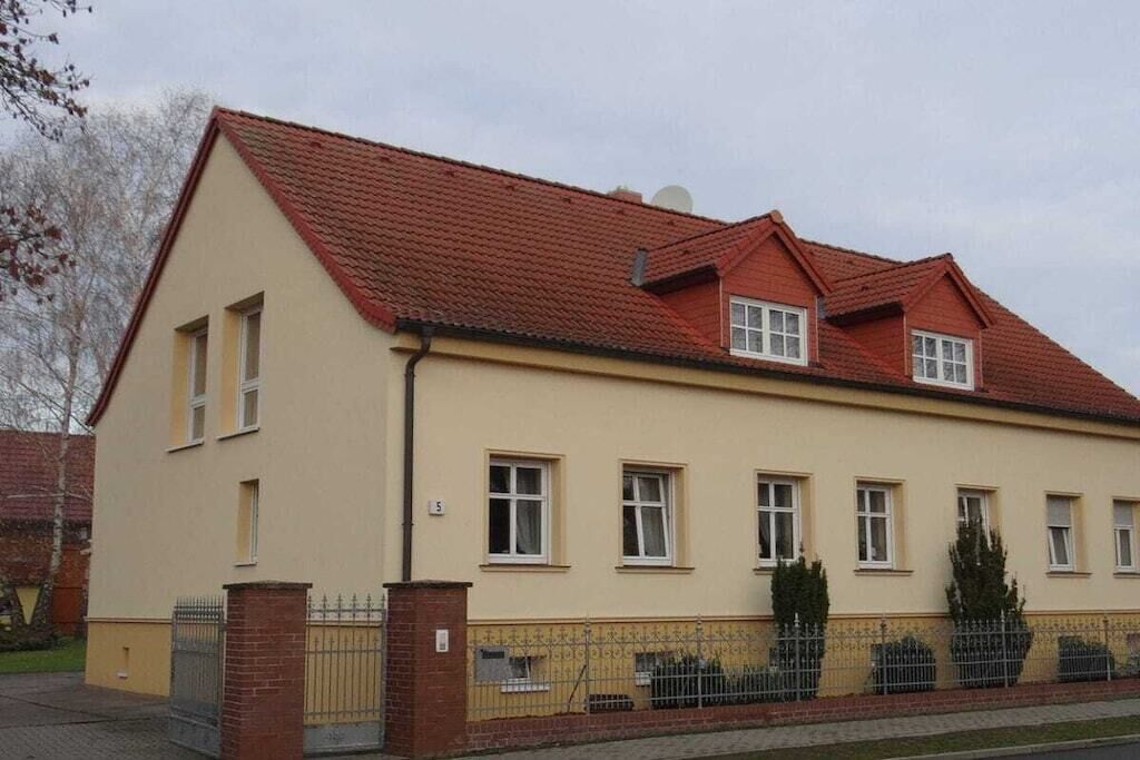 Ein zweistöckiges Gebäude mit rotem Ziegeldach, zahlreichen Fenstern und einem umzäunten Grundstück.