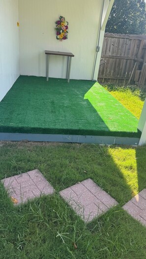 Eine Terrassenfläche mit Kunstgrasanlage, einer Bank und einem Holzzaun.