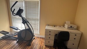 A room with a stationary bike, a desk with drawers, and a printer. - Spacious 4-bedroom house in fantastic Columbus with AC and gym (Columbus)