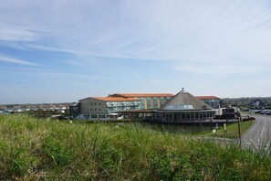 A modern building with a prominent glass facade and a unique conical roof structure. - Strandslag Juliana 139 (Julianadorp aan Zee)