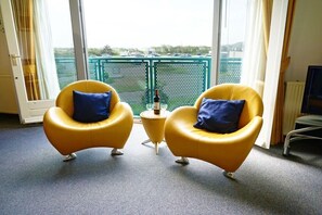 Ein Zimmer mit zwei gelben Sesseln, einem kleinen Beistelltisch und Blick durch große Fenster.