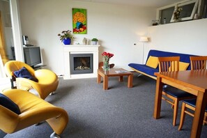 Ein Wohnzimmer mit Kamin, gelben Sesseln, einem blauen Sofa und einem Holzessttisch.