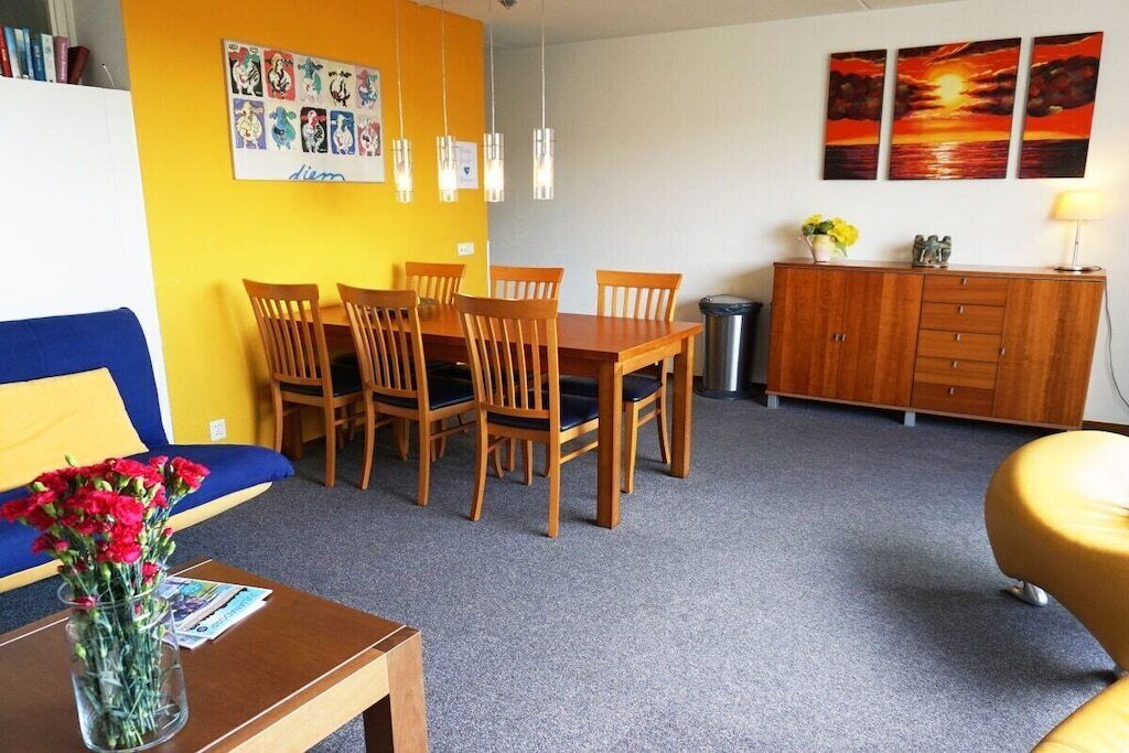 A room with a dining table and chairs, a sofa, a cabinet, and artwork on the walls.