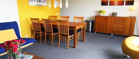 A room with a dining table and chairs, a sofa, a cabinet, and artwork on the walls.